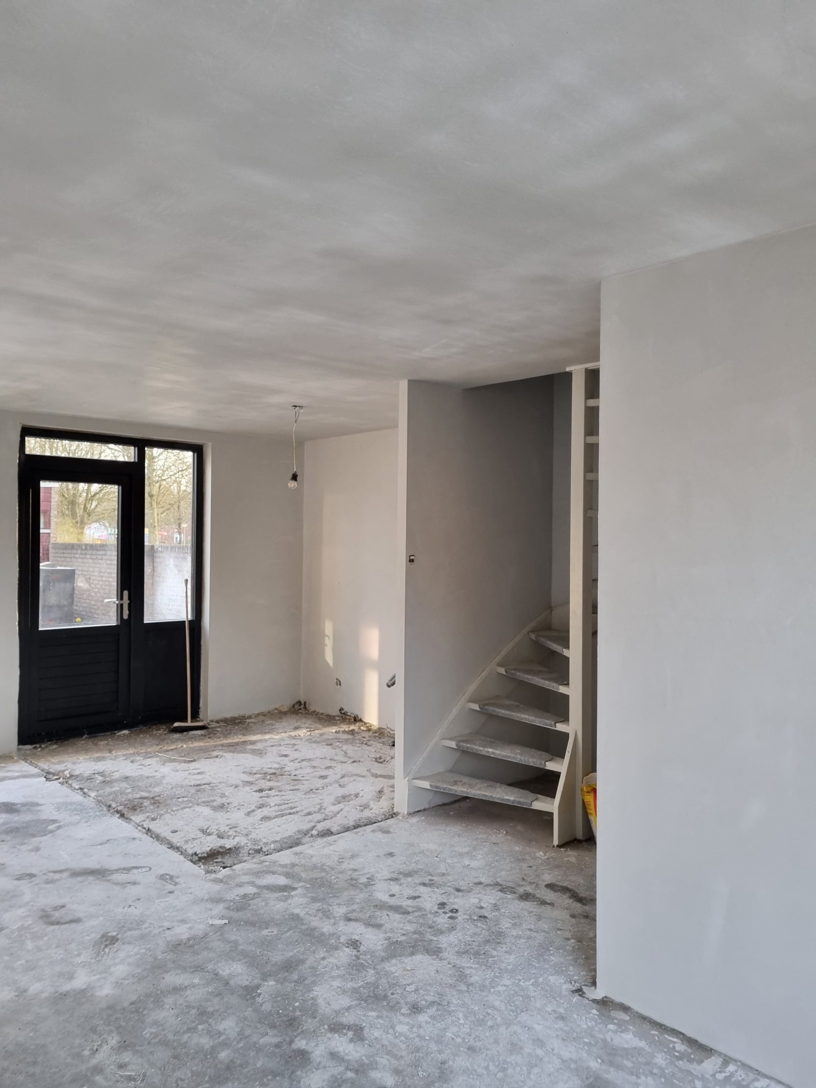 Woonruimte in de ruwbouw, vers gestuct, met nieuwe kozijnen en een open trap
