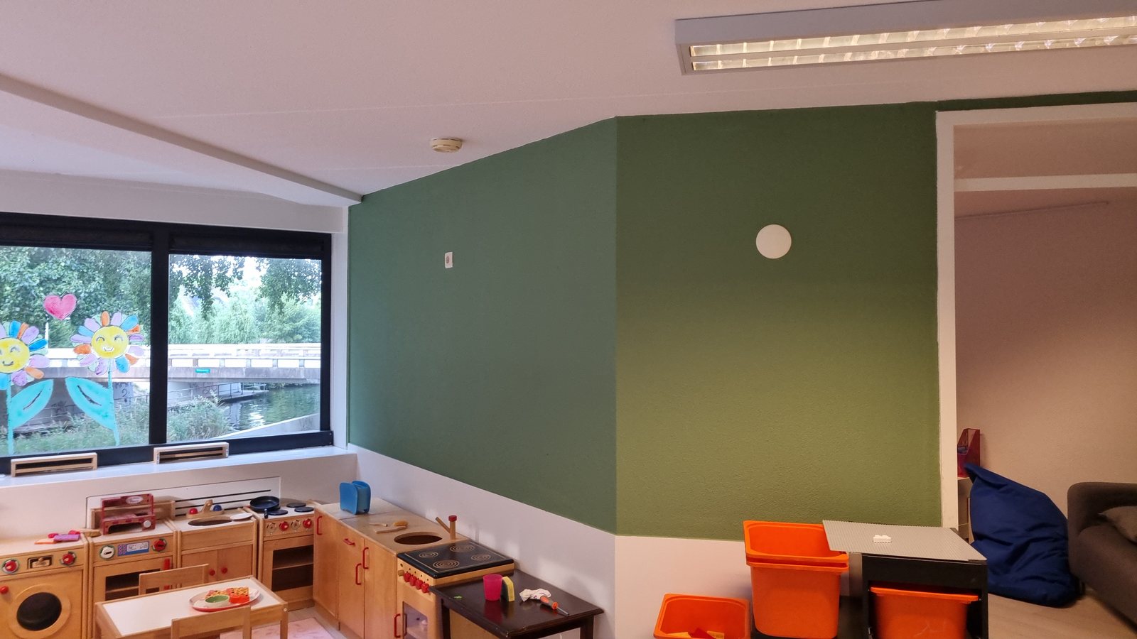 Ingerichte groepsruimte met groene wand, keukenblok en speelhoek